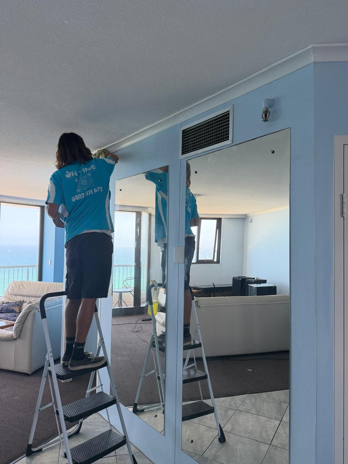Blue On Time cleaner wiping mirror wall and cornices in a Surfers Paradise apartment